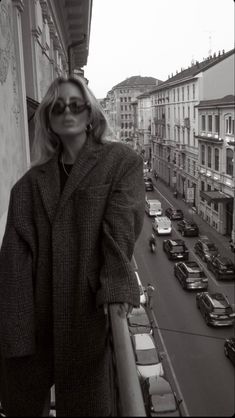 a woman standing on the balcony of a building with cars parked in front of her