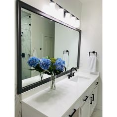 a bathroom with two sinks and a large mirror on the wall above it is decorated with blue hydrangeas