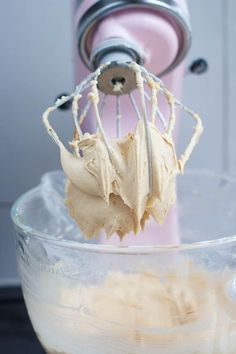 a whisk in a glass bowl next to a pink mixer with white icing