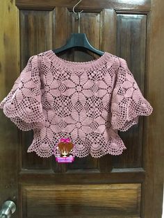 a pink crocheted sweater hanging on a wooden door