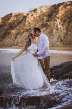 a bride and groom are standing on the rocks by the water at their beach wedding