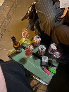 two people sitting at a table with beer cans and other items on it, next to a backpack