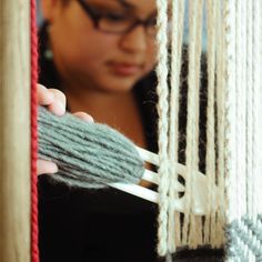 a woman is weaving yarn on a loom with her hands and eyeglasses