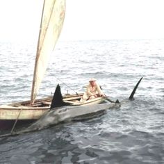 a man sitting on top of a small boat in the middle of the ocean with a sail