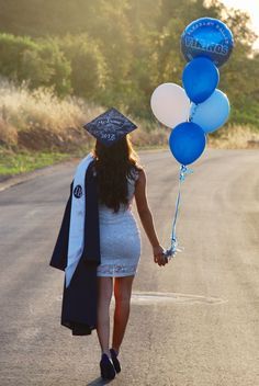 a woman walking down the road with balloons attached to her head and graduation cap on