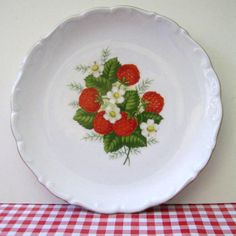 a white plate with strawberries and flowers on it sitting on a checkered tablecloth