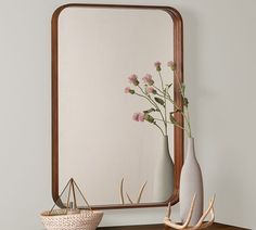 a mirror and vase with flowers in it on a table next to a basket full of antlers