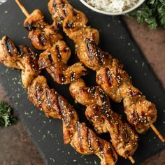 chicken skewers with sesame seeds and rice on a cutting board