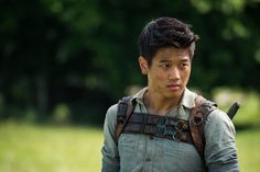 a young man in overalls with a backpack on his back walking through the grass