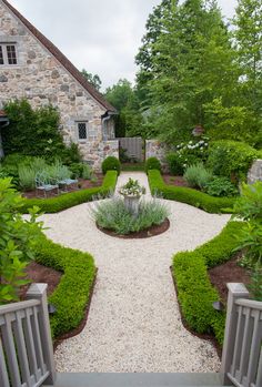 a stone house surrounded by lush green trees and shrubbery, with a gravel path leading to the front door