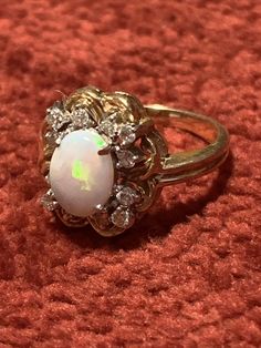 an opal and diamond ring sitting on top of a red carpeted surface,