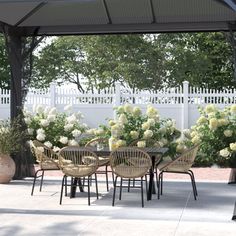 an outdoor dining area with tables and chairs under a pergolated roof, surrounded by white hydrangeas