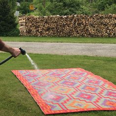 a person is spraying water on a colorful blanket in the grass with a hose attached to it