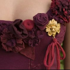 a close up of a purple dress with flowers on the side and a gold brooch