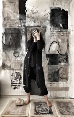 a woman standing in front of a wall covered in graffiti and holding her hands up to her face