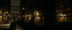 people sitting at tables in a library with bookshelves and lamps on the walls