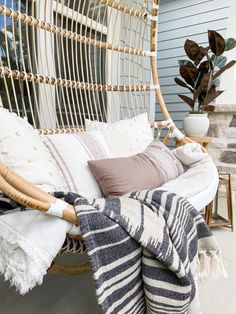 a wicker hammock with pillows and blankets on the back porch, next to a potted plant