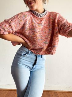 a woman in jeans and a sweater is posing with her arms behind her back,