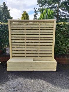 a wooden bench sitting in front of a hedge next to a wall with slats on it