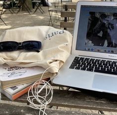 an open laptop computer sitting on top of a wooden table next to books and glasses