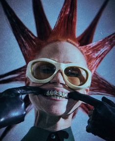 a woman with long red hair and goggles holding a toothbrush in front of her mouth