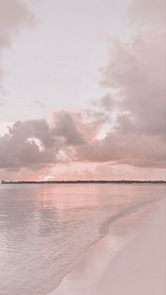 the water is calm and pink as the sun sets on the horizon in the distance