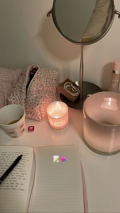 a desk with a candle, mirror and notebook on it