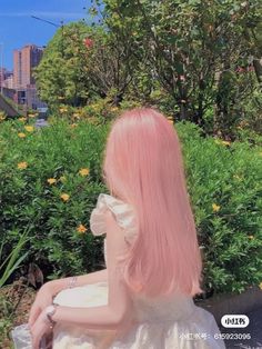 a woman with pink hair sitting on a bench in front of some bushes and flowers