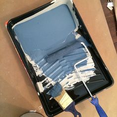 the paint is blue and white on the table next to some brushes in a black tray