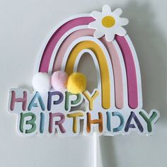 a happy birthday cake topper with a rainbow and pom poms on it