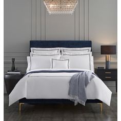 a bed with white sheets and blue pillows in a gray room next to a night stand