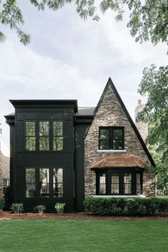 a black house with lots of windows on the front and side of it, surrounded by green grass