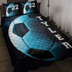 a bed covered in a blue and black comforter with soccer balls printed on it