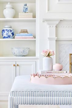 a white and blue striped ottoman with pink flowers on it in front of a fireplace