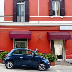 a small blue car parked in front of a red building with shutters on the windows