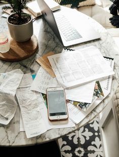 a table topped with lots of papers and a cell phone next to a laptop computer