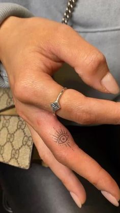 a woman's hand with a small tattoo on the middle finger and an eye ring