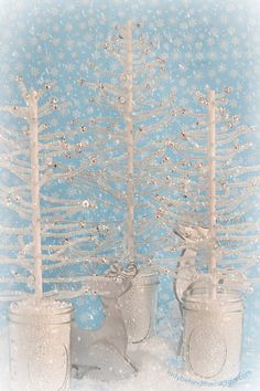 two small white christmas trees in buckets with snowflakes on the wall behind them