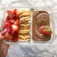 a person holding a container with chocolate dip and strawberries