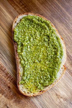 a piece of bread with pesto on it sitting on top of a wooden table