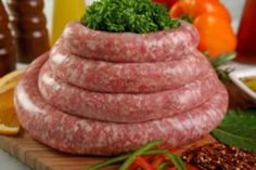 a pile of sausage sitting on top of a wooden cutting board next to other foods