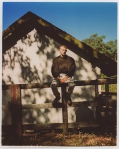 a man sitting on top of a wooden fence next to a white building with a roof