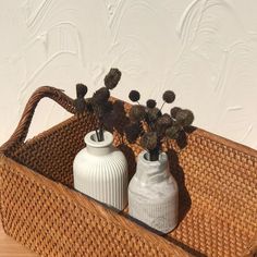 two white vases sitting on top of a wicker basket