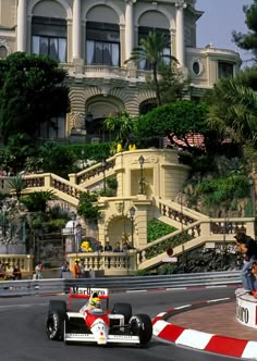 a man driving a race car down a street next to a tall building with stairs