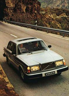 an old volvo car driving down the road with mountains in the backgrouund