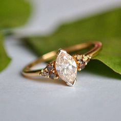 an engagement ring with two pear shaped diamonds on top of it, sitting next to a green leaf