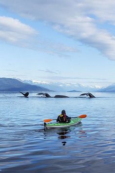 a person in a kayak paddling on the water with mountains in the background