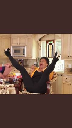 two women sitting at a kitchen table with their arms in the air and one woman standing up