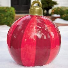 a large red ball ornament sitting on top of snow in front of a house