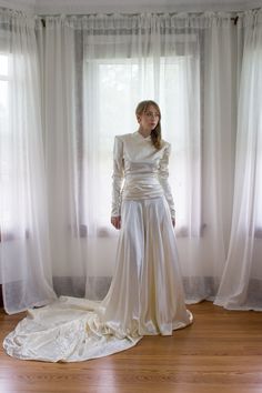 a woman standing in front of a window wearing a white dress